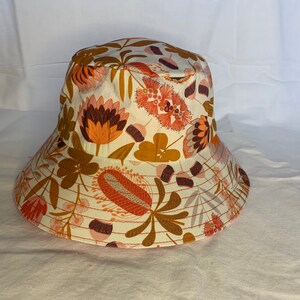 May include: A white bucket hat with a floral print featuring orange, brown, and pink flowers. The hat has a wide brim and a flat crown.