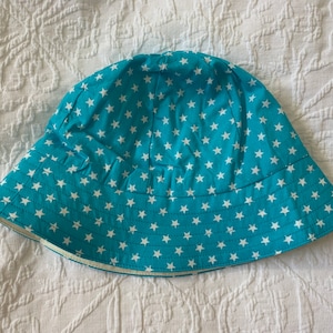 May include: A turquoise blue bucket hat with a white star pattern. The hat has a wide brim and a flat crown.