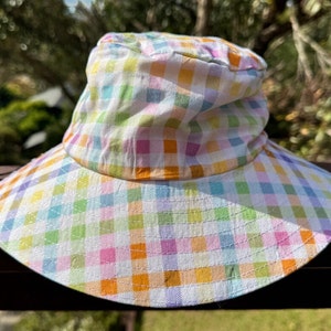 May include: A white bucket hat with a colorful checkered pattern in shades of pink, orange, green, blue, and yellow.