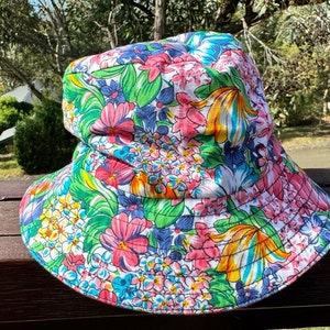 May include: A white bucket hat with a colorful floral print. The print features pink, blue, yellow, and green flowers on a white background.