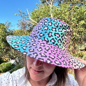 May include: A wide-brimmed hat with a rainbow ombre leopard print. The hat is made of a soft, lightweight fabric and has a comfortable fit.