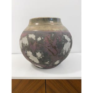May include: A round ceramic vase with a wide body and a narrow neck. The vase features a colour palette of purple, grey, white, and brown. The design includes a mottled pattern with cloud-like shapes, creating a unique decorative piece.