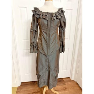 May include: A vintage olive green two-piece dress with a ruffled neckline and long sleeves. The sleeves are adorned with small bows. The dress features a fitted bodice and a long skirt. The outfit is displayed on a mannequin.
