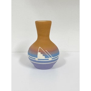May include: A small decorative vase with a rounded body and a narrow neck. The vase has a colour gradient from brown to blue, with a lavender base. A white geometric design is painted on the blue section.