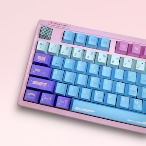 May include: A pink and blue mechanical keyboard with custom keycaps featuring various symbols and designs. The keyboard has a light blue space bar and a pink frame.