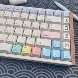 May include: A pastel-colored mechanical keyboard with a wooden frame. The keyboard has white, pink, blue, and yellow keys. The word "hello" is printed on a pink key. A dog icon is on a key.