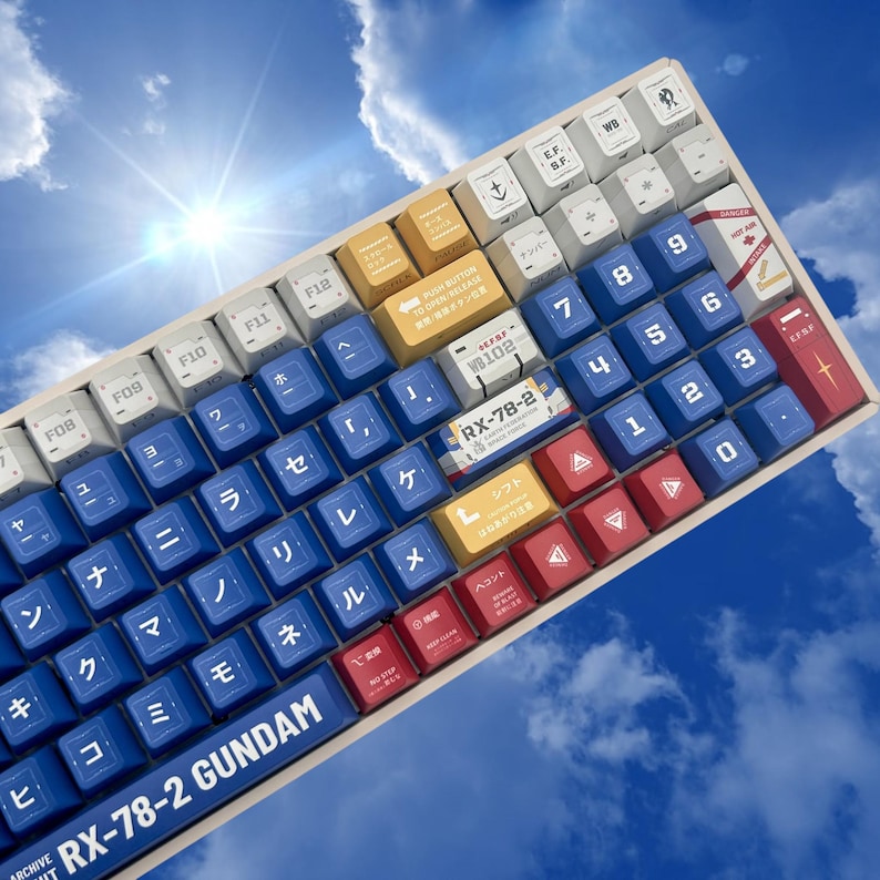Puede incluir: Un teclado mec&aacute;nico con teclas azules, blancas, amarillas y rojas. El teclado tiene caracteres japoneses y el texto "RX-78-2 GUNDAM" en la barra espaciadora. El fondo es un cielo azul con nubes.