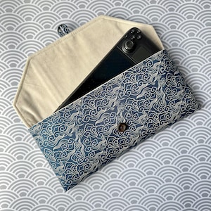 May include: A blue and white patterned fabric clutch with a button closure. The clutch is open and a black gaming console is inside.