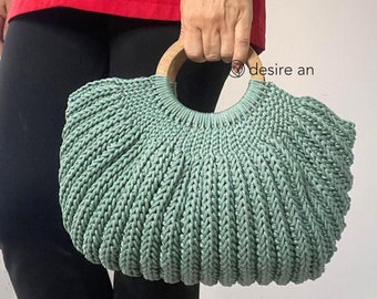 May include: A light green crocheted bag with a wooden handle. The bag is round and has a textured design.