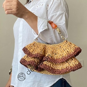 May include: A brown and tan woven straw bag with a ruffled trim. The bag has a brown and orange beaded strap.