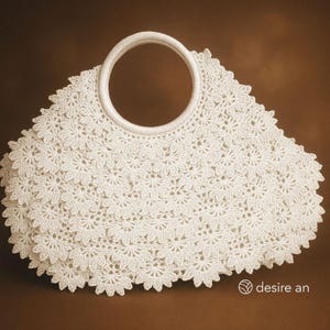 May include: A white, crocheted handbag with a circular handle. The bag features a floral pattern and a scalloped edge. The handle is also white and appears to be made of a woven material. The bag is set against a brown background.