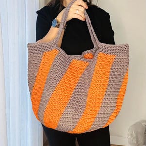 May include: A large, crocheted tote bag with orange and gray stripes. The bag has a wide, flat base and two long handles.