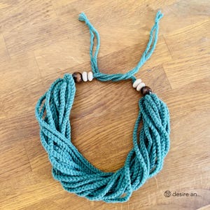 Può includere: Una collana all'uncinetto blu turchese con perline di legno. La collana è realizzata con più fili di filo e ha un design semplice.