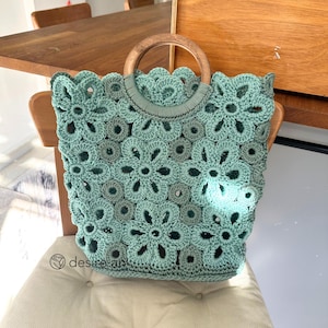 May include: A light green crocheted tote bag with a wooden handle. The bag has a floral pattern and is perfect for carrying everyday essentials.