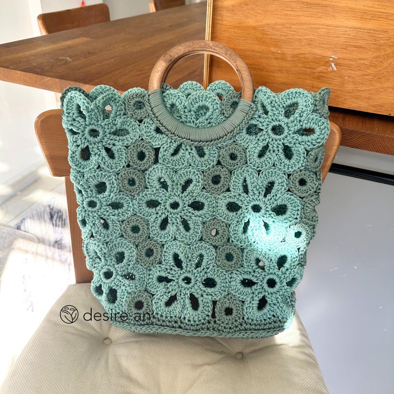 May include: A light green crocheted tote bag with a wooden handle. The bag has a floral pattern and is perfect for carrying everyday essentials.
