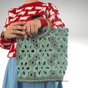 May include: A teal crocheted bag with a wooden handle. The bag is made of a delicate, floral pattern.