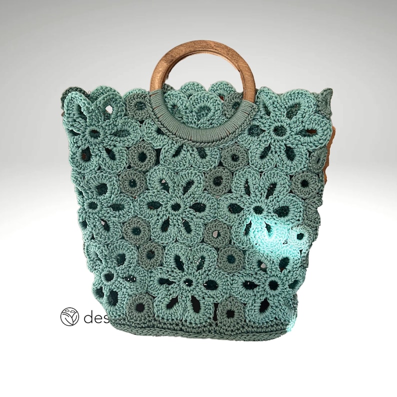 May include: A teal crochet tote bag with a wooden handle. The bag is made of a delicate, floral pattern.