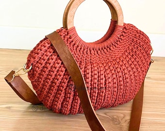 May include: A crocheted handbag with a brown leather strap and a wooden handle. The bag is a reddish-orange color.