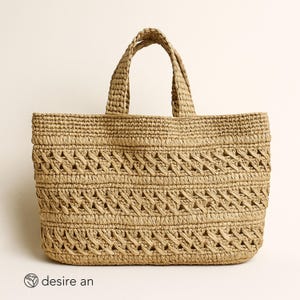 May include: A beige woven tote bag with two handles. The bag has a rectangular shape and a decorative woven pattern across the front. The brand name "desire an" is visible in the lower left corner.