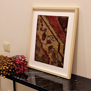 May include: A framed print of a vintage rug with a red, brown, and beige pattern. The frame is a light wood color and the print is on a white background.