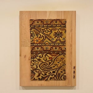 May include: A close-up of a framed piece of art featuring a colorful patterned rug on a wooden background. The text "From the Past" is visible in the lower right corner of the frame.