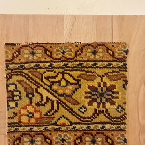 May include: A close-up of a colorful rug with intricate floral patterns in shades of brown, yellow, orange, and blue. The rug is framed by a wooden border.