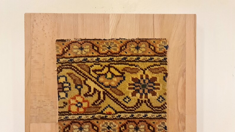 May include: A close-up of a colorful rug with intricate floral patterns in shades of brown, yellow, orange, and blue. The rug is framed by a wooden border.