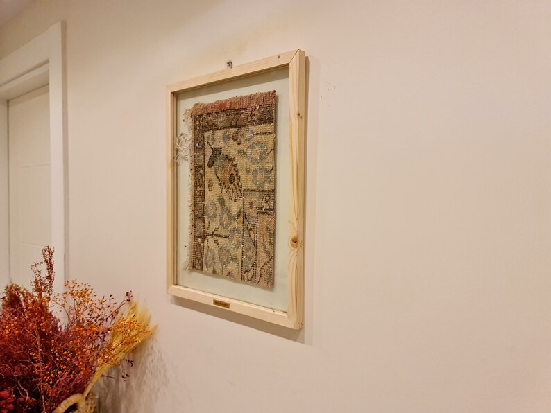 May include: A framed piece of antique fabric with a faded floral pattern in shades of brown, blue, and white. The fabric is displayed behind glass in a simple wooden frame.