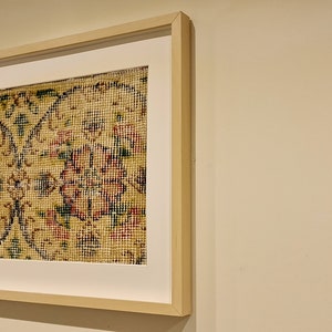 May include: A framed artwork featuring a close-up of a patterned rug with intricate floral designs in shades of red, green, and yellow.