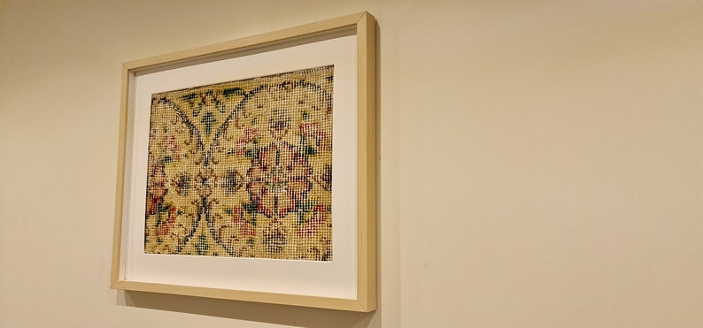 May include: A framed artwork featuring a close-up of a patterned rug with intricate floral designs in shades of red, green, and yellow.