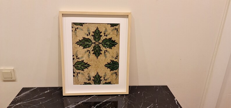 May include: A framed print of a vintage rug with a green and beige floral pattern.