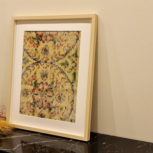 May include: A framed print of a vintage rug with a floral pattern in shades of red, green, and yellow. The rug is displayed on a black table.