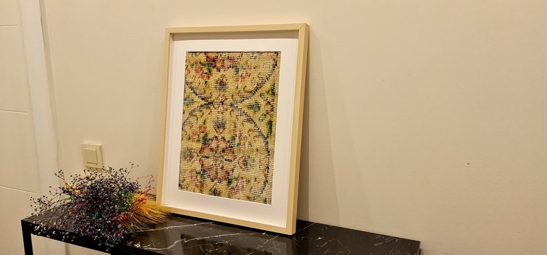 May include: A framed print of a vintage rug with a floral pattern in shades of red, green, and yellow. The rug is displayed on a black table.