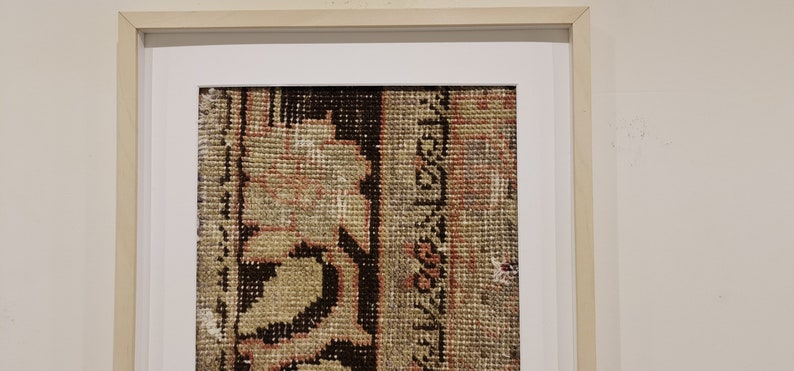 K&ouml;nnte beinhalten: Ein gerahmter Vintage-Teppich mit einem detaillierten Blumenmuster in Braun-, Beige- und Rosat&ouml;nen. Der Teppich ist in einem einfachen Holzrahmen mit einer wei&szlig;en Passepartout gerahmt.