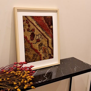 May include: A framed print of a vintage rug with a red, brown, and beige pattern. The print is hanging on a wall above a black marble table.