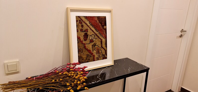 May include: A framed print of a vintage rug with a red, brown, and beige pattern. The print is hanging on a wall above a black marble table.
