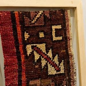 May include: A framed piece of antique fabric with a red, brown, and white geometric pattern. The fabric is woven with a variety of textures and colors.