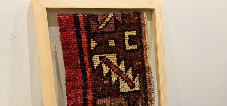 May include: A framed piece of antique fabric with a red, brown, and white geometric pattern. The fabric is woven with a variety of textures and colors.