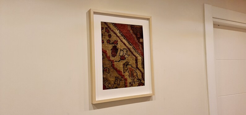 May include: A framed print of a close-up of a colorful rug with intricate patterns in shades of red, brown, and gold.