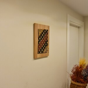 Puede incluir: Una pieza de arte de tela colorida enmarcada con un patr&oacute;n geom&eacute;trico cuelga de una pared beige claro en un pasillo.