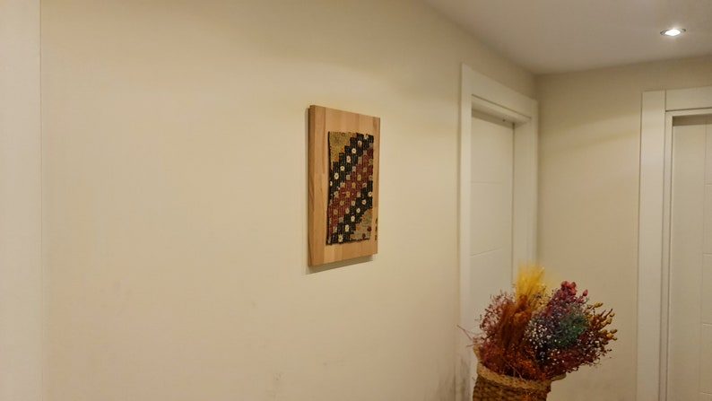 Puede incluir: Una pieza de arte de tela colorida enmarcada con un patr&oacute;n geom&eacute;trico cuelga de una pared beige claro en un pasillo.