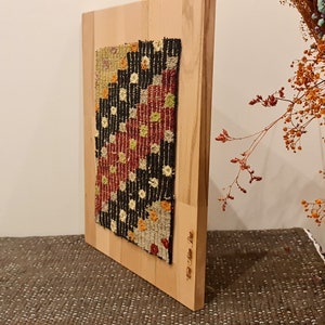 Puede incluir: Un tapiz enmarcado con un patr&oacute;n geom&eacute;trico en tonos de rojo, negro, blanco y amarillo. El tapiz est&aacute; montado en un marco de madera.