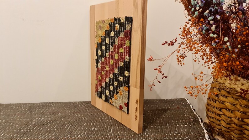 Puede incluir: Un tapiz enmarcado con un patr&oacute;n geom&eacute;trico en tonos de rojo, negro, blanco y amarillo. El tapiz est&aacute; montado en un marco de madera.