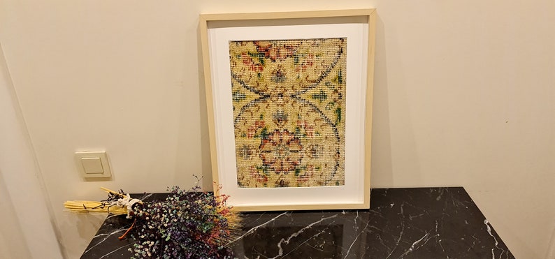 May include: A framed print of a vintage rug with a floral pattern in shades of red, yellow, green, and blue. The rug is framed in a light wood frame.