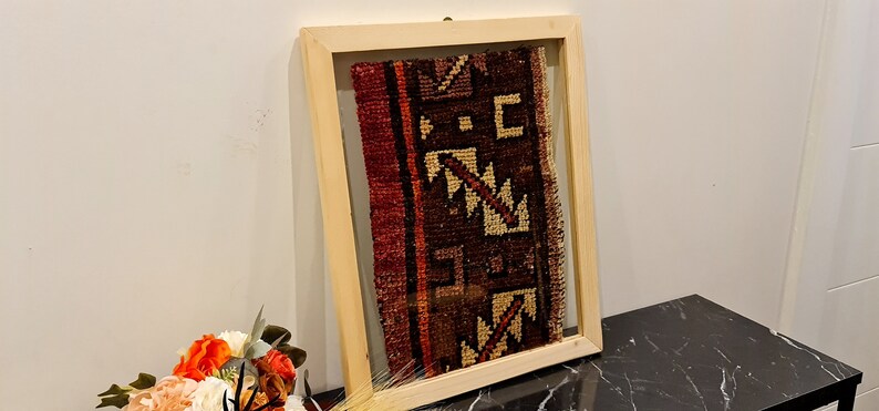May include: A framed piece of antique fabric with a geometric pattern in shades of red, brown, and cream. The fabric is displayed in a natural wood frame with a glass front.