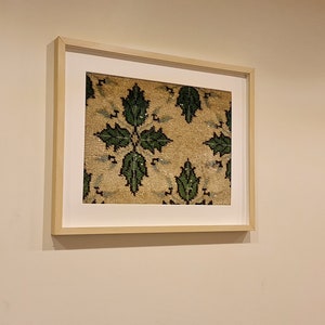 May include: A framed print of a vintage rug with a repeating pattern of green leaves on a beige background.