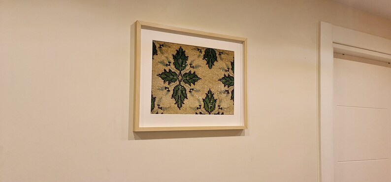 May include: A framed print of a vintage rug with a repeating pattern of green leaves on a beige background.