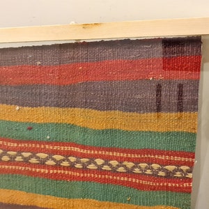 May include: A framed colorful woven tapestry with a wood frame. The tapestry has stripes of red, yellow, green, and purple.