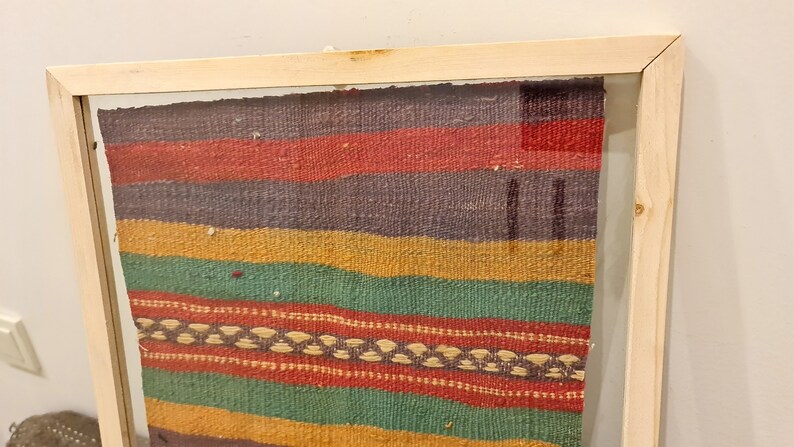 May include: A framed colorful woven tapestry with a wood frame. The tapestry has stripes of red, yellow, green, and purple.