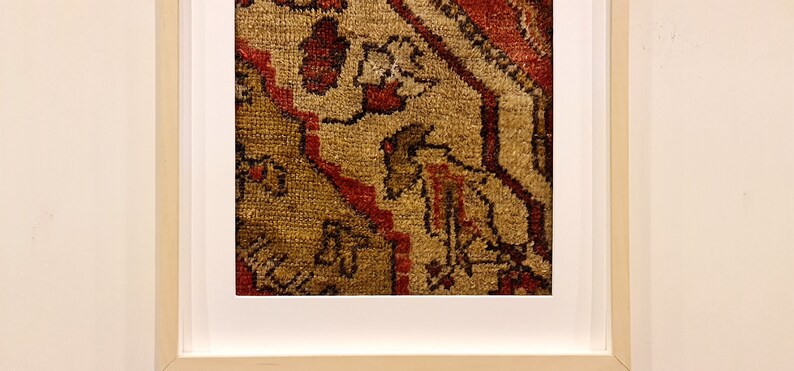 May include: Close-up of a framed rug with a detailed pattern of red, brown, and beige. The rug has a geometric design with intricate details.